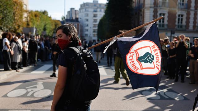 Ein Schüler mit halb vermummtem Gesicht trägt eine Fahne mit einem Logo der Schul-Proteste