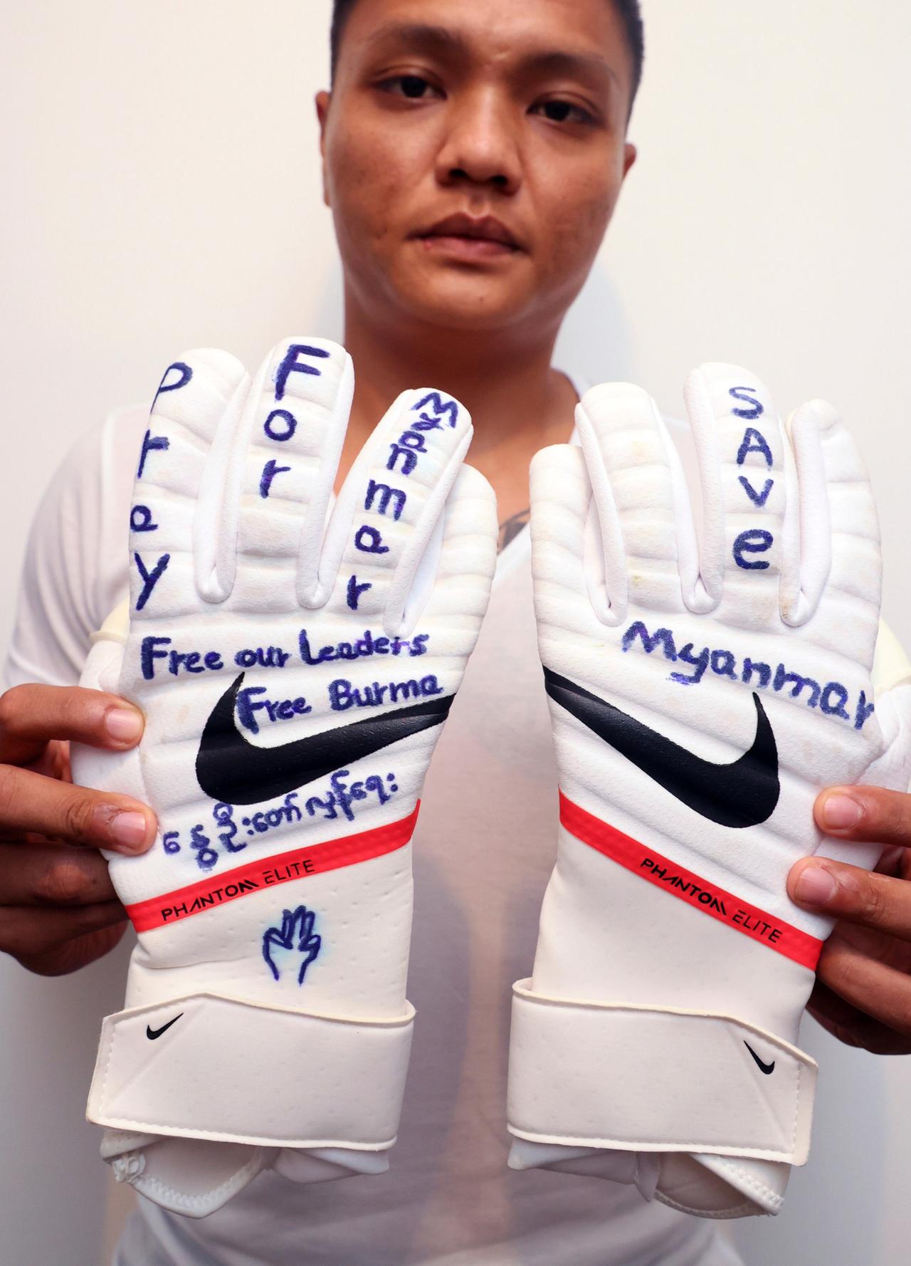 Der ehemalige Fußballnationaltorhüter Myanmars, Pyae Lyan Aung, hält seine Torwarthandschuhe in die Kamera. Auf ihnen steht "Freies Myanmar" geschrieben.