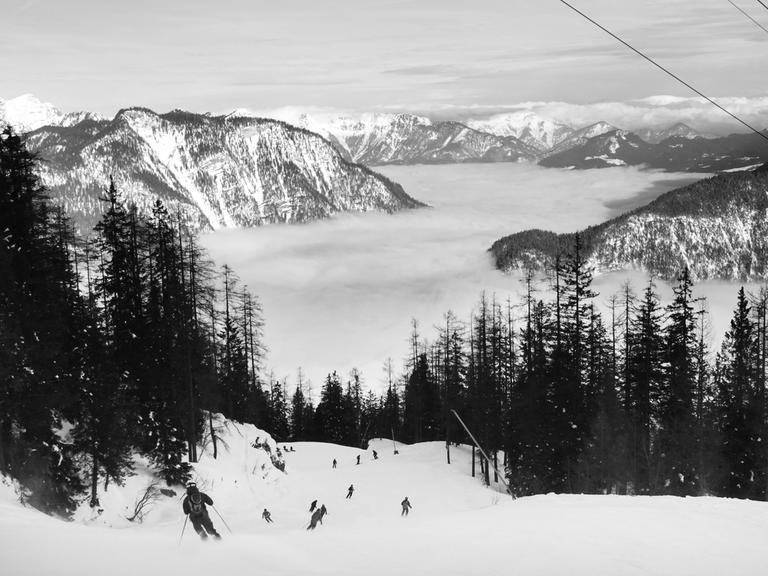 Schwarz-weiß Foto: Menschen fahren Ski am Krippenstein. Blick auf die Piste und das Panorama, wolkenverhangende Berge.