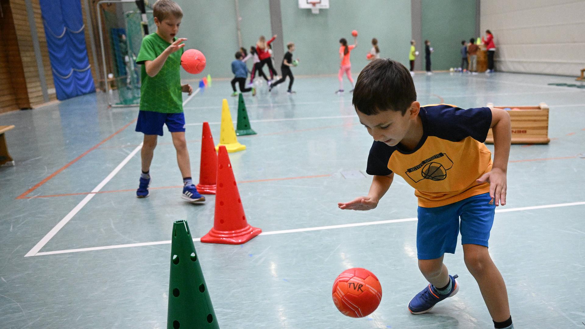 Kinder dribbeln beim Grundschulaktionstag mit einem Handball um Pyloren herum.