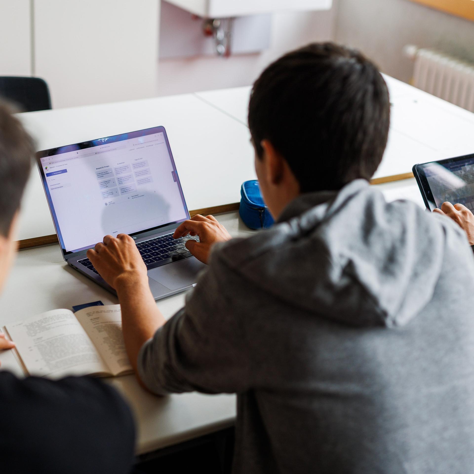Schüler eines Gymnasiums sitzen vor einem Laptop und benutzen ein KI-Tool. 