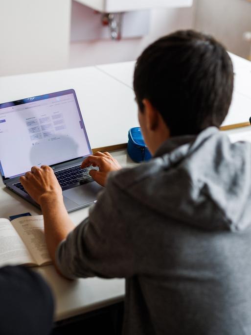 Schüler eines Gymnasiums sitzen vor einem Laptop und benutzen ein KI-Tool. 