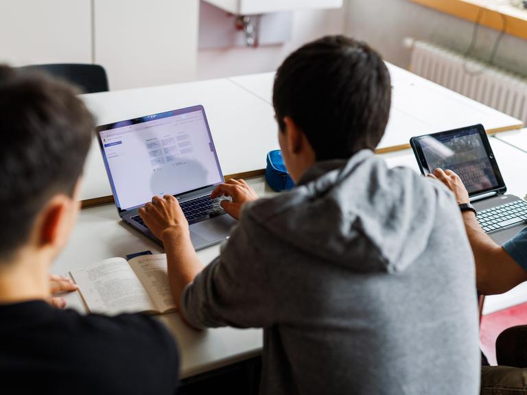 Schüler eines Gymnasiums sitzen vor einem Laptop und benutzen ein KI-Tool. 