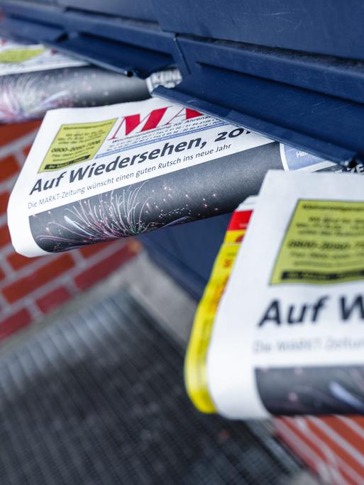 Mehrere Anzeigenblätter schauen aus blauen Briefkastenschlitzen hervor.