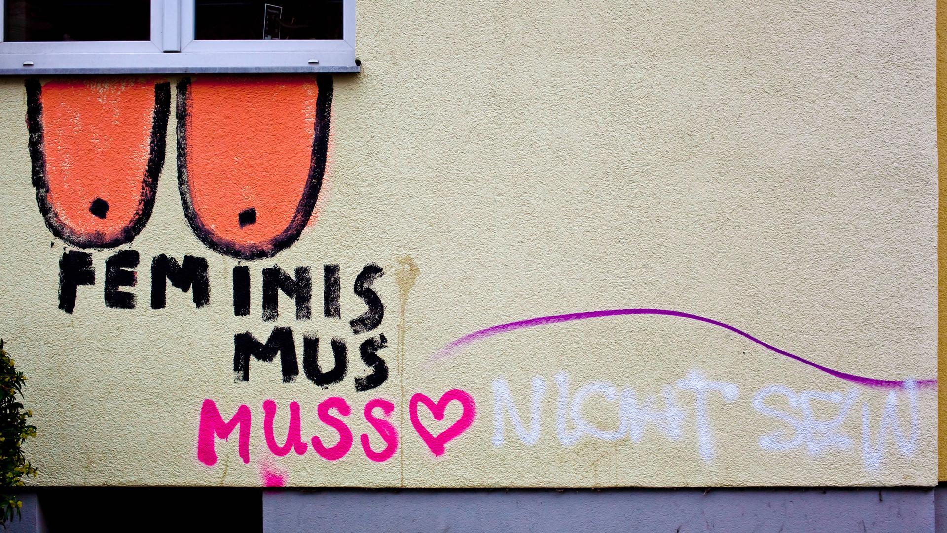 An einer Wand ist ein Grafitto gesprüht mit "Feminismus muss" und der Ergänzung "nicht sein". Dazu wurden Brüste gemalt.