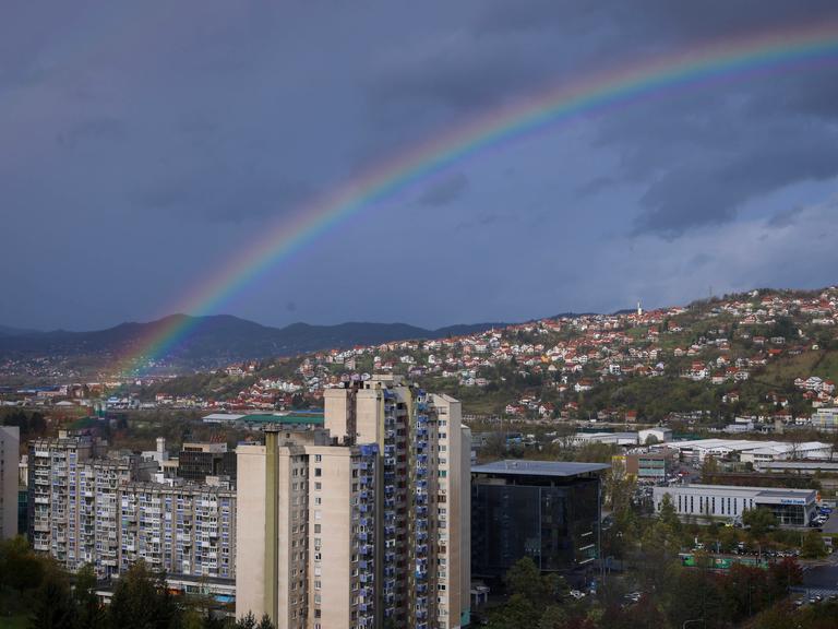 Blick auf die bosnische Hauptstadt Sarajewo über der gerade ein Regenbogen zu sehen ist. 