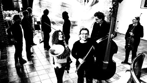 Ensemblemusiker stehen mit ihren Instrumenten im Kirchenraum verteilt. 