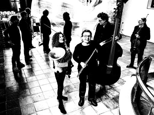 Ensemblemusiker stehen mit ihren Instrumenten im Kirchenraum verteilt. 