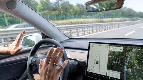 Ein Mann sitzt in einem auf der Autobahn fahrenden Auto und nimmt die Hände vom Steuer.