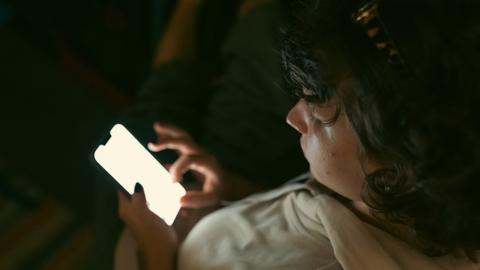 Ein Kind sitzt in dunkler Umgebung und schaut auf das Display seines Smartphones.