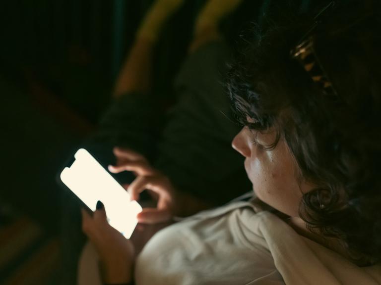Ein Kind sitzt in dunkler Umgebung und schaut auf das Display seines Smartphones. Ein Kind sitzt in dunkler Umgebung und schaut auf das Display seines Smartphones.