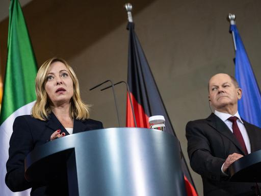 Die italienische Ministerpräsidentin Giorgia Meloni und Bundeskanzler Olaf Scholz stehen an Pulten. Im Hintergrund die Fahnen von Italien, Deutschland und EU.