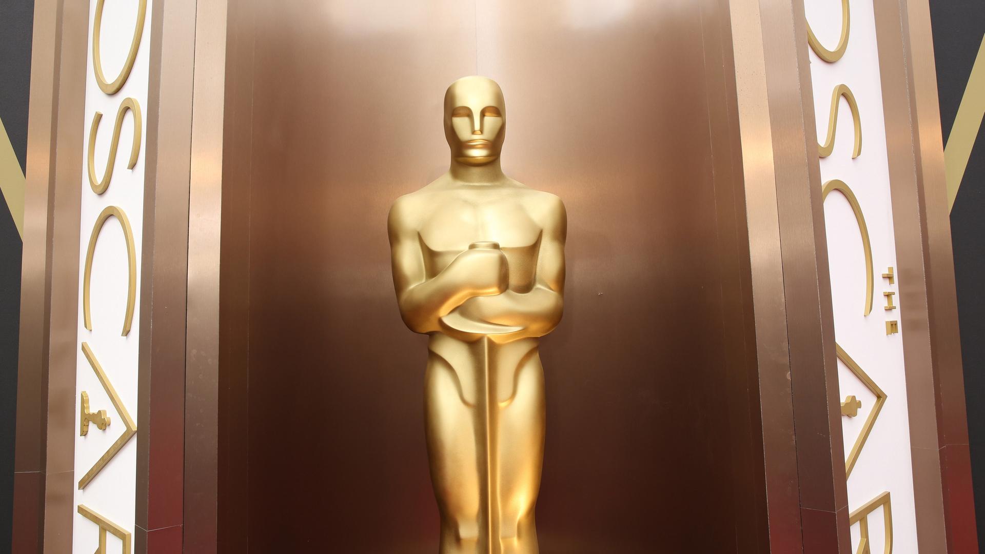 Eine große Oscar-Statue zwischen zwei senkrechten Schildern, auf denen "The Oscars" steht.