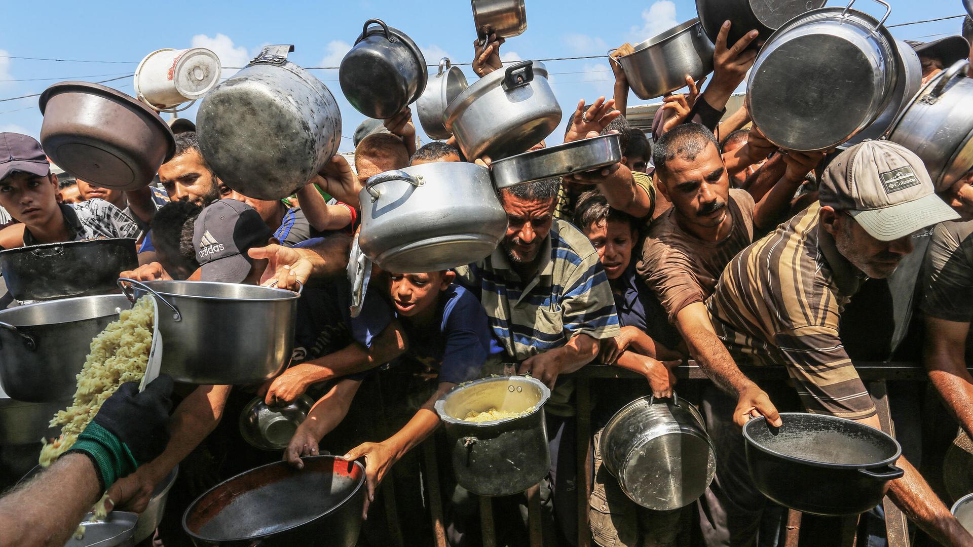Palästinenser, darunter auch Kinder, die aufgrund der Blockade Israels und der Angriffe auf den Gazastreifen Schwierigkeiten haben, sich mit Lebensmitteln zu versorgen, stehen Schlange, um warme Mahlzeiten zu erhalten. Palästinenser, darunter auch Kinder, die aufgrund der Blockade Israels und der Angriffe auf den Gazastreifen Schwierigkeiten haben, sich mit Lebensmitteln zu versorgen, stehen Schlange, um warme Mahlzeiten zu erhalten.