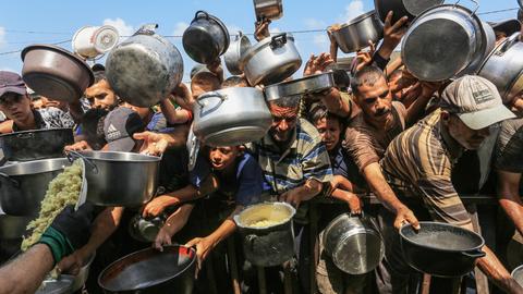 Palästinenser, darunter auch Kinder, die aufgrund der Blockade Israels und der Angriffe auf den Gazastreifen Schwierigkeiten haben, sich mit Lebensmitteln zu versorgen, stehen Schlange, um warme Mahlzeiten zu erhalten.