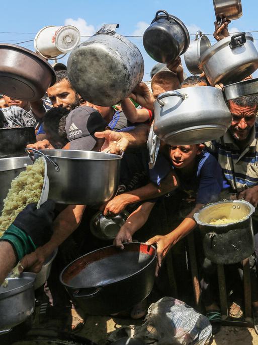 Palästinenser, darunter auch Kinder, die aufgrund der Blockade Israels und der Angriffe auf den Gazastreifen Schwierigkeiten haben, sich mit Lebensmitteln zu versorgen, stehen Schlange, um warme Mahlzeiten zu erhalten.