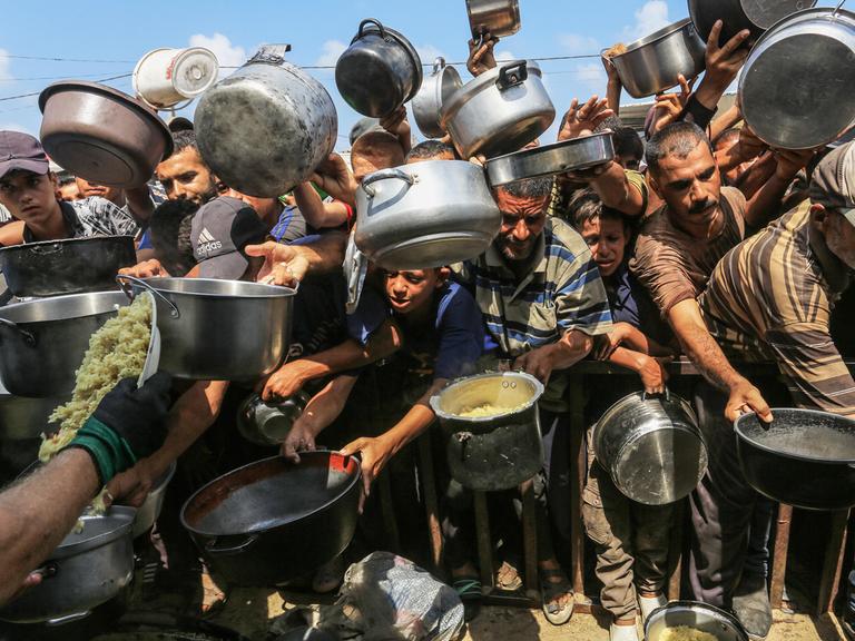 Palästinenser, darunter auch Kinder, die aufgrund der Blockade Israels und der Angriffe auf den Gazastreifen Schwierigkeiten haben, sich mit Lebensmitteln zu versorgen, stehen Schlange, um warme Mahlzeiten zu erhalten.