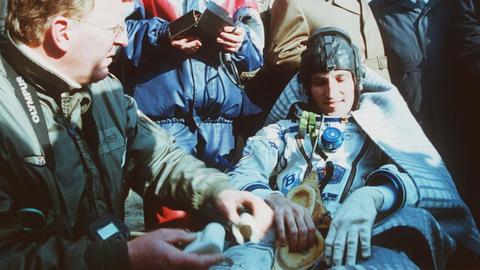 Der österreichische Astronaut Franz Viehböck nach der Landung am 10. Oktober 1991 in der Steppe von Kasachstan. Er ist sitzend im Raumfahreranzug, umgeben von anderen Personen. 