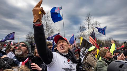 Eine Gruppe von US-Amerikanern sind zu einer Kundgebung versammelt. Sie scheinen wütend und aufgebracht zu sein. Eine Person in der Mitte hält schreiend den Mittelfinger in die Luft.
