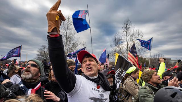 Eine Gruppe von US-Amerikanern sind zu einer Kundgebung versammelt. Sie scheinen wütend und aufgebracht zu sein. Eine Person in der Mitte hält schreiend den Mittelfinger in die Luft.
