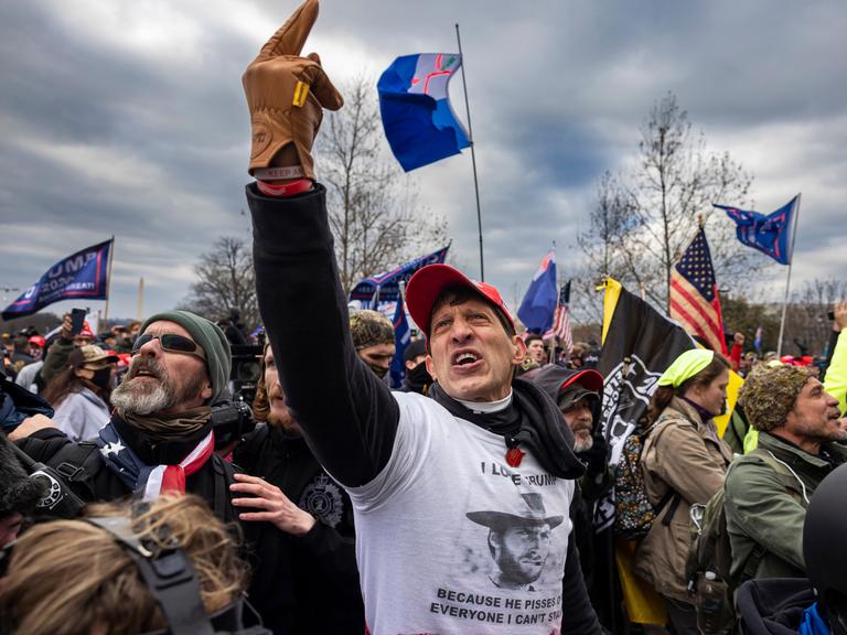 Eine Gruppe von US-Amerikanern sind zu einer Kundgebung versammelt. Sie scheinen wütend und aufgebracht zu sein. Eine Person in der Mitte hält schreiend den Mittelfinger in die Luft. Eine Gruppe von US-Amerikanern sind zu einer Kundgebung versammelt. Sie scheinen wütend und aufgebracht zu sein. Eine Person in der Mitte hält schreiend den Mittelfinger in die Luft.