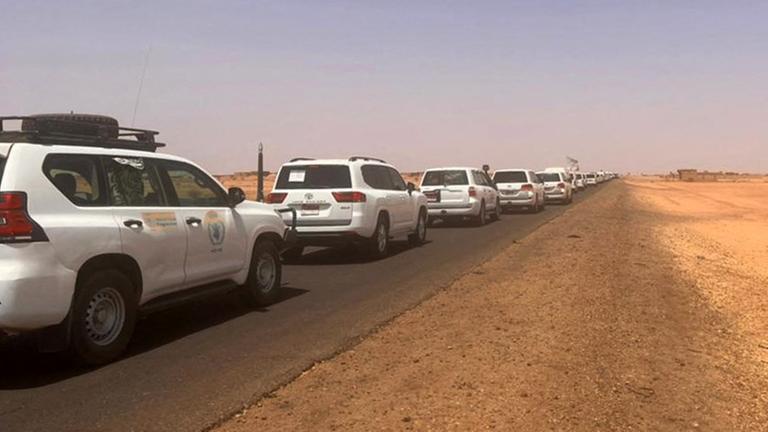 Zu sehen ist ein Fahrzeugkonvoi in der sudanesischen Wüste auf dem Weg zum Hafen Port Sudan. Menschen fliehen vor den Kämpfen im Sudan.