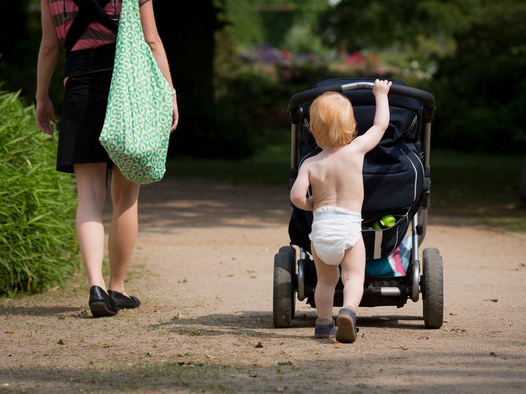 Ein Kleinkind mit Windel schiebt seinen Kinderwagen durch einen Park. Ein Kleinkind mit Windel schiebt seinen Kinderwagen durch einen Park.