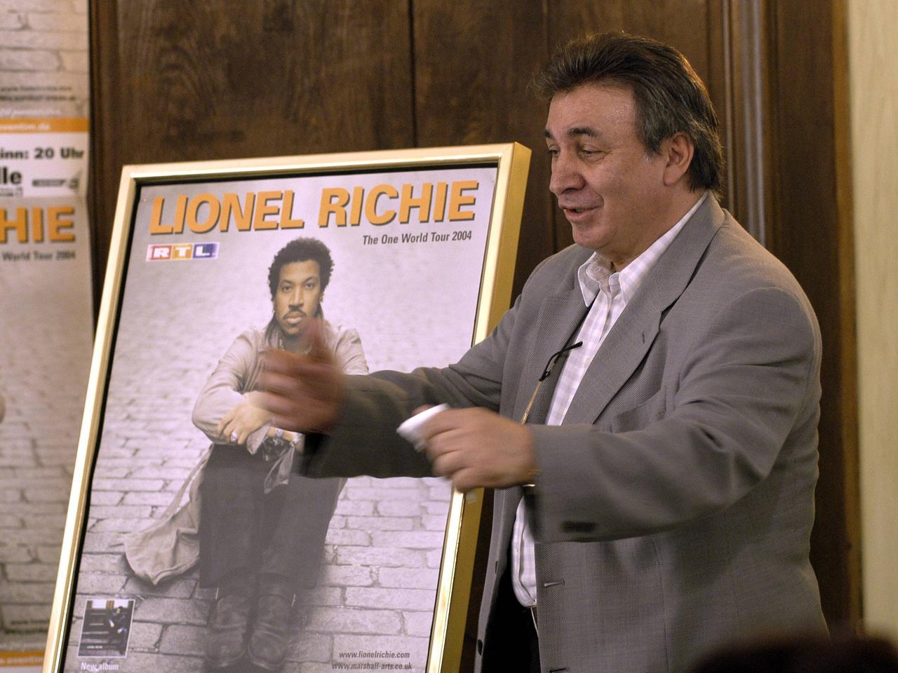 Marcel Avram hält ein Konzertplakat des Sängers Lionel Ritchie in die Kamera