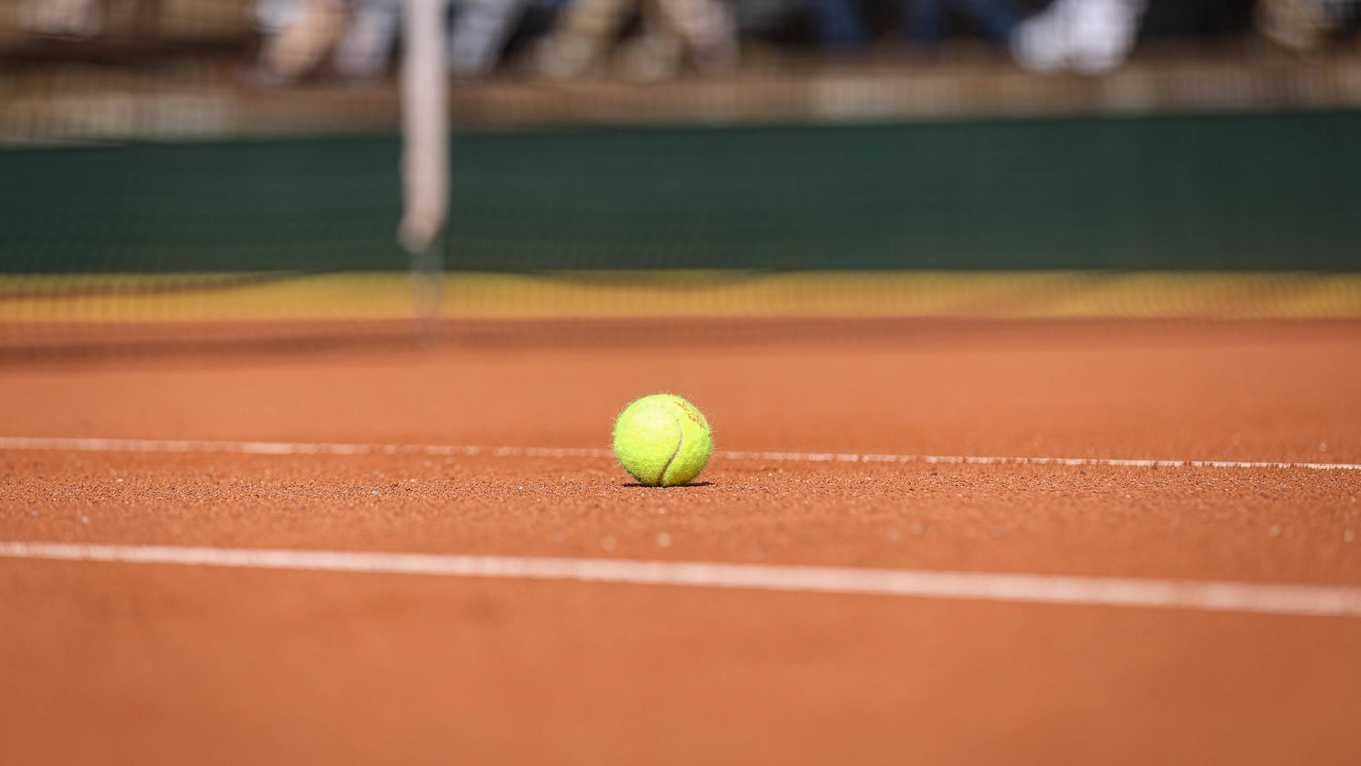 Ein Tennisball liegt auf einem Sandplatz.