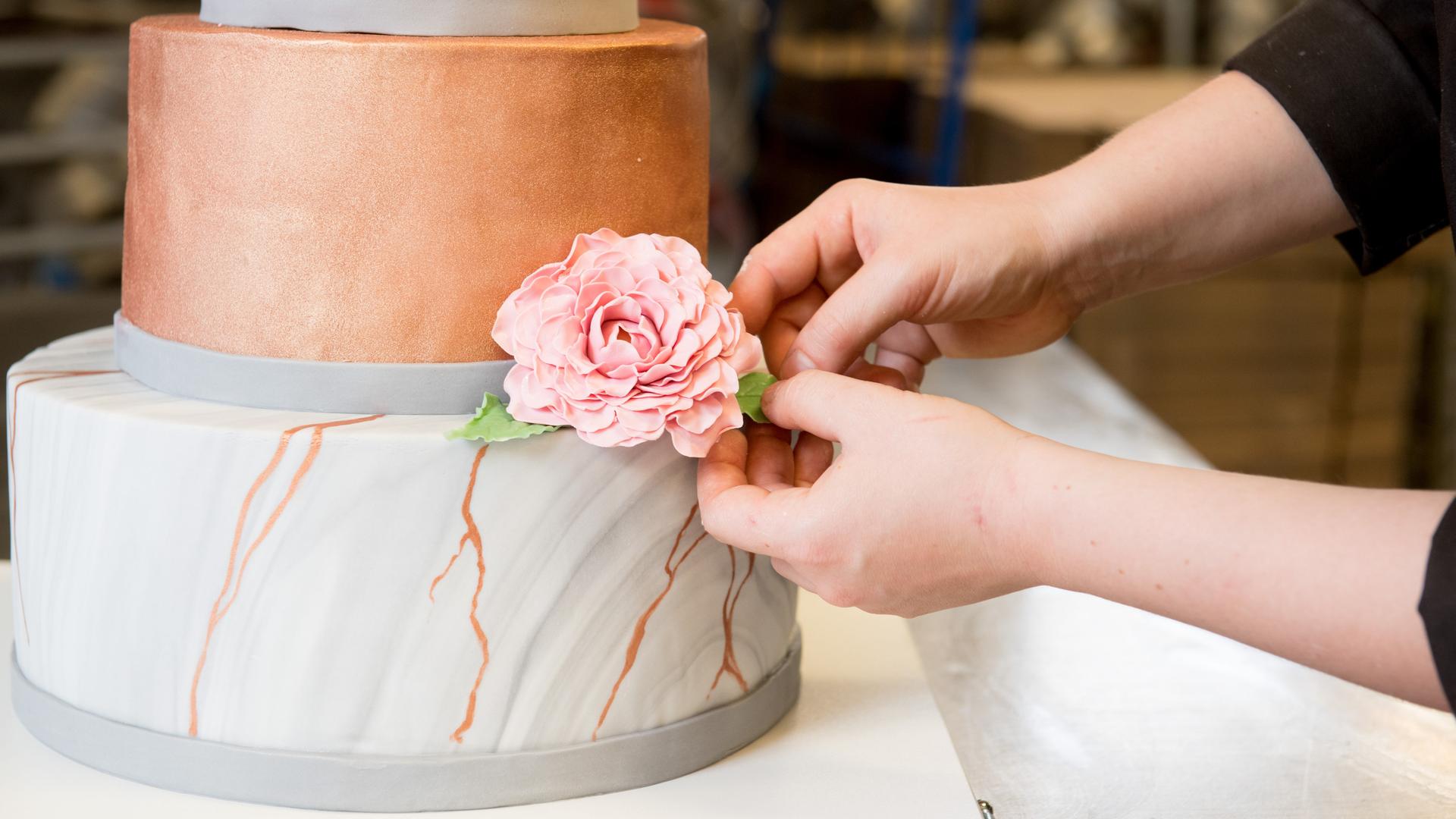 Eine angehende Konditorin dekoriert eine Hochzeitstorte mit Rosenblaettern aus Modelierschokolade.