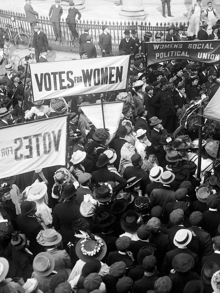 In London demonstrieren im Jahr 1910 Frauenrechtlerinnen vor der Queen's Hall. Sie tragen Banner, die das Wahlrecht für Frauen einfordern. 

