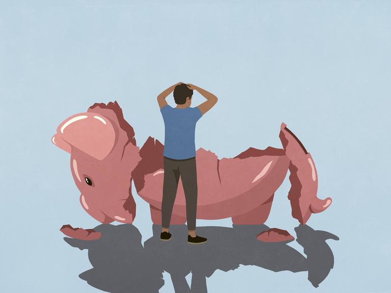 Ein gestresster Mann schaut auf ein übergroßes leeres zerschlagenes Sparschwein.