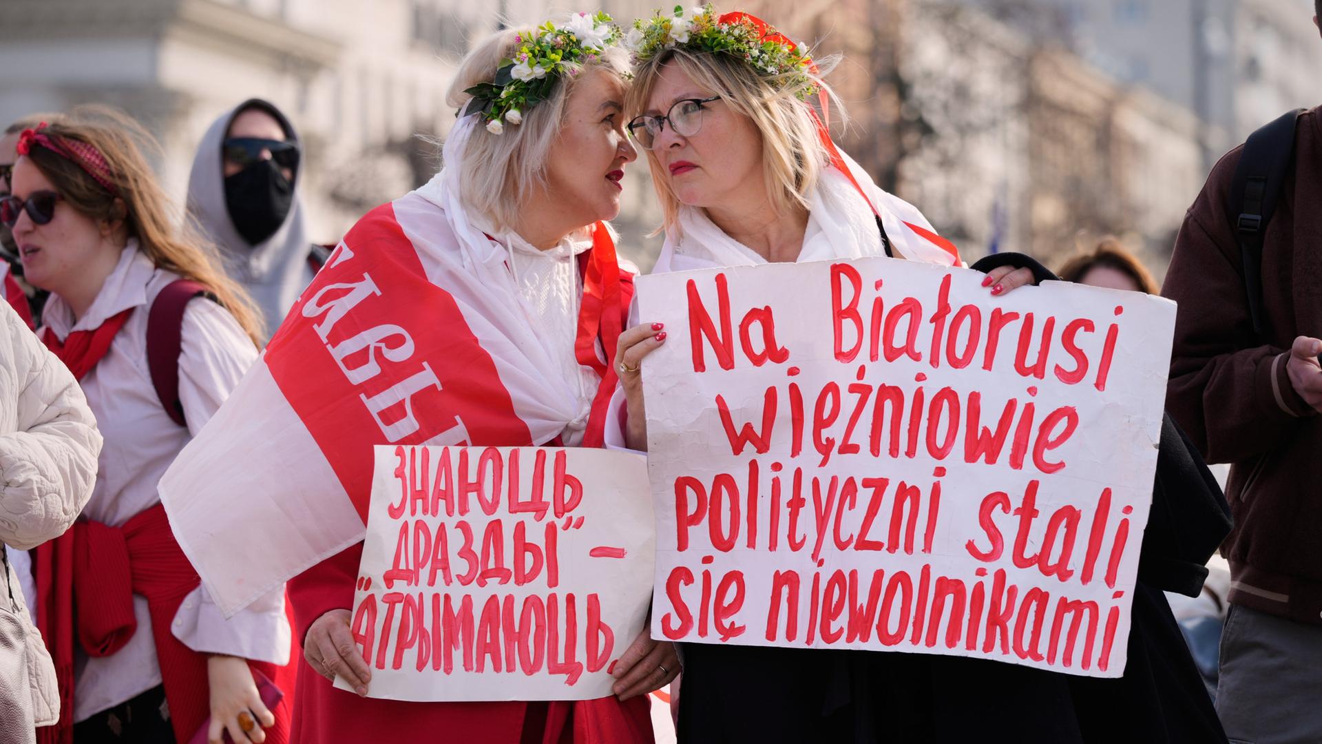 Teilnehmende einer oppossitionellen Demonstration in Warschau. Zwei Frauen tragen weiß-rot-weiße Flaggen sowie Plakate in belarrusischer und polnischer Sprache. Teilnehmende einer oppossitionellen Demonstration in Warschau. Zwei Frauen tragen weiß-rot-weiße Flaggen sowie Plakate in belarrusischer und polnischer Sprache.