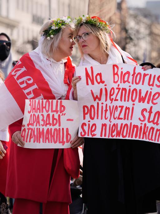 Teilnehmende einer oppossitionellen Demonstration in Warschau. Zwei Frauen tragen weiß-rot-weiße Flaggen sowie Plakate in belarrusischer und polnischer Sprache.
