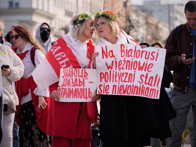 Teilnehmende einer oppossitionellen Demonstration in Warschau. Zwei Frauen tragen weiß-rot-weiße Flaggen sowie Plakate in belarrusischer und polnischer Sprache.
