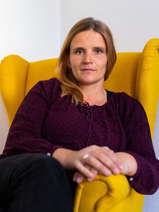 Sarah Pohl sitzt in einem gelben Sessel in ihrem Büro. 