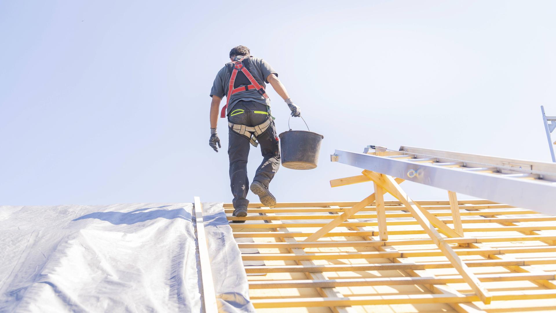 Ein Arbeiter in Sicherheitskleidung klettert eine Leiter hoch, um auf einem Dach zu arbeiten, bei sonnigem Wetter, Dachsanierung, Hausbau, 