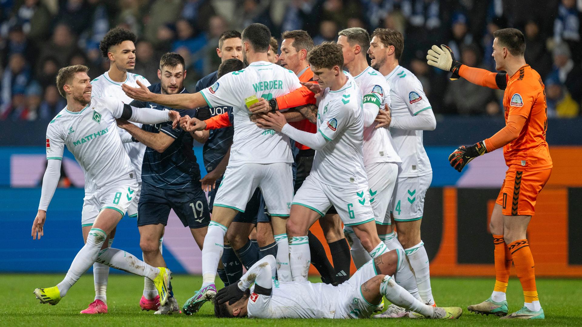 Mehrere Spieler stehen auf dem Spielfeld beisammen und argumentieren sichtlich empört. Mehrere Spieler stehen auf dem Spielfeld beisammen und argumentieren sichtlich empört.