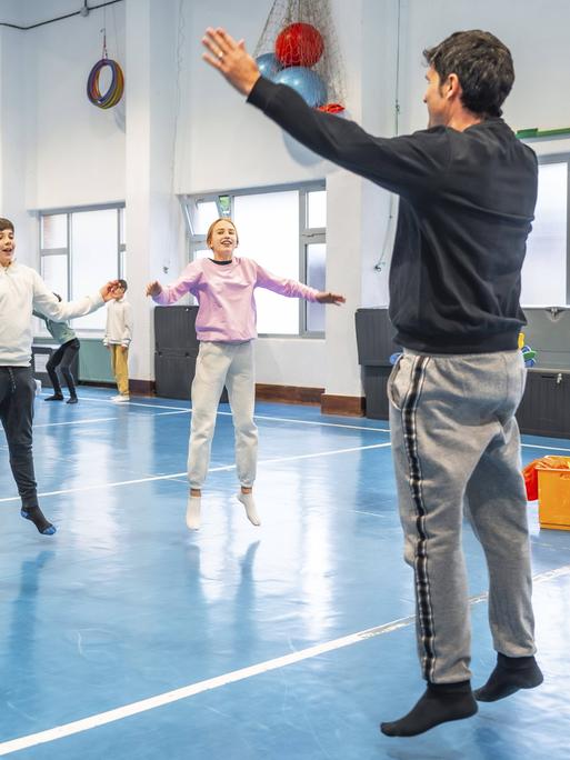 Symbolbild: Schüler machen zusammen mit ihrem Sportlehrer in der Schule Hampelmänner und Fitnessübungen.