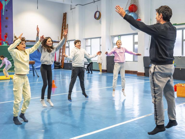 Symbolbild: Schüler machen zusammen mit ihrem Sportlehrer in der Schule Hampelmänner und Fitnessübungen.