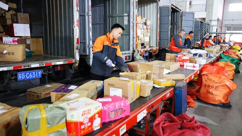 Mitarbeiter sortieren Expresspakete auf automatisierten Sortierlinien in einem Verteilzentrum in China, dahinter sind geöffnete LKW für den Transport. Mitarbeiter sortieren Expresspakete auf automatisierten Sortierlinien in einem Verteilzentrum in China, dahinter sind geöffnete LKW für den Transport.