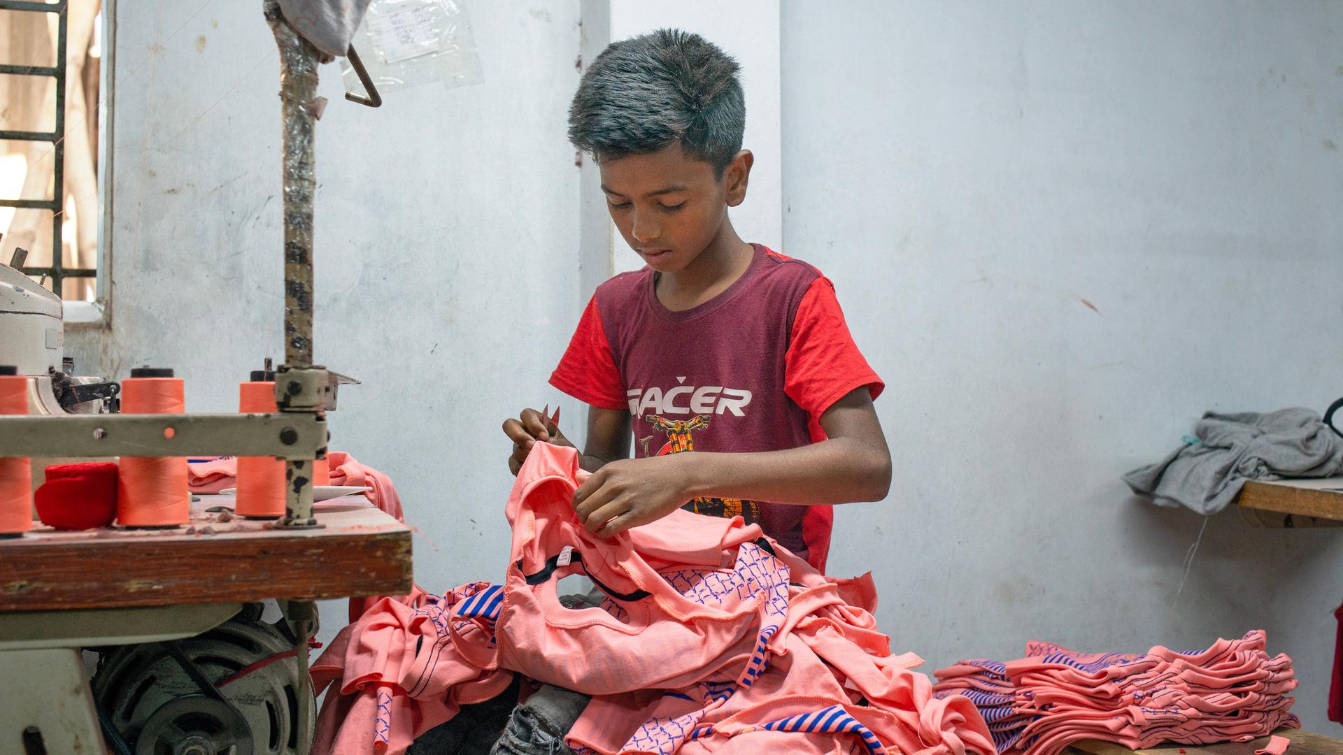 In Bangladesch näht ein Kind in einer Textilfabrik Stoffe zusammen. 