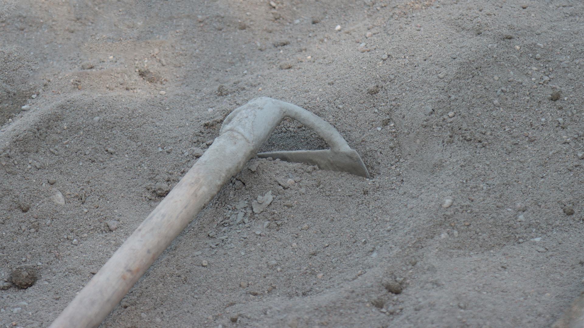 Ein Haufen Sand, in dem eine Schüppe steckt.