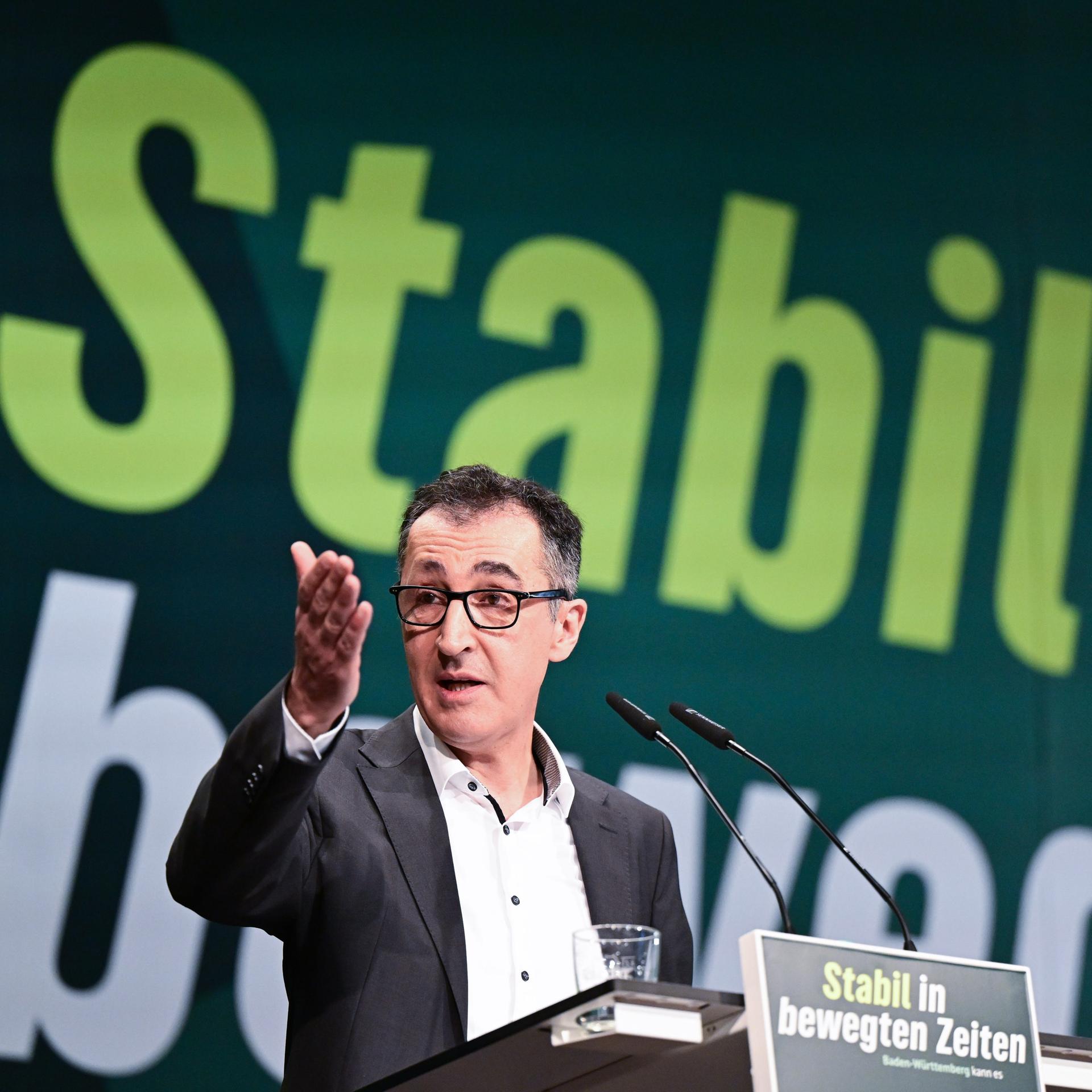 Ein Mann im Anzug und mit Brille steht an einem Rednerpult. Er spricht und gestikuliert mit einer Hand.