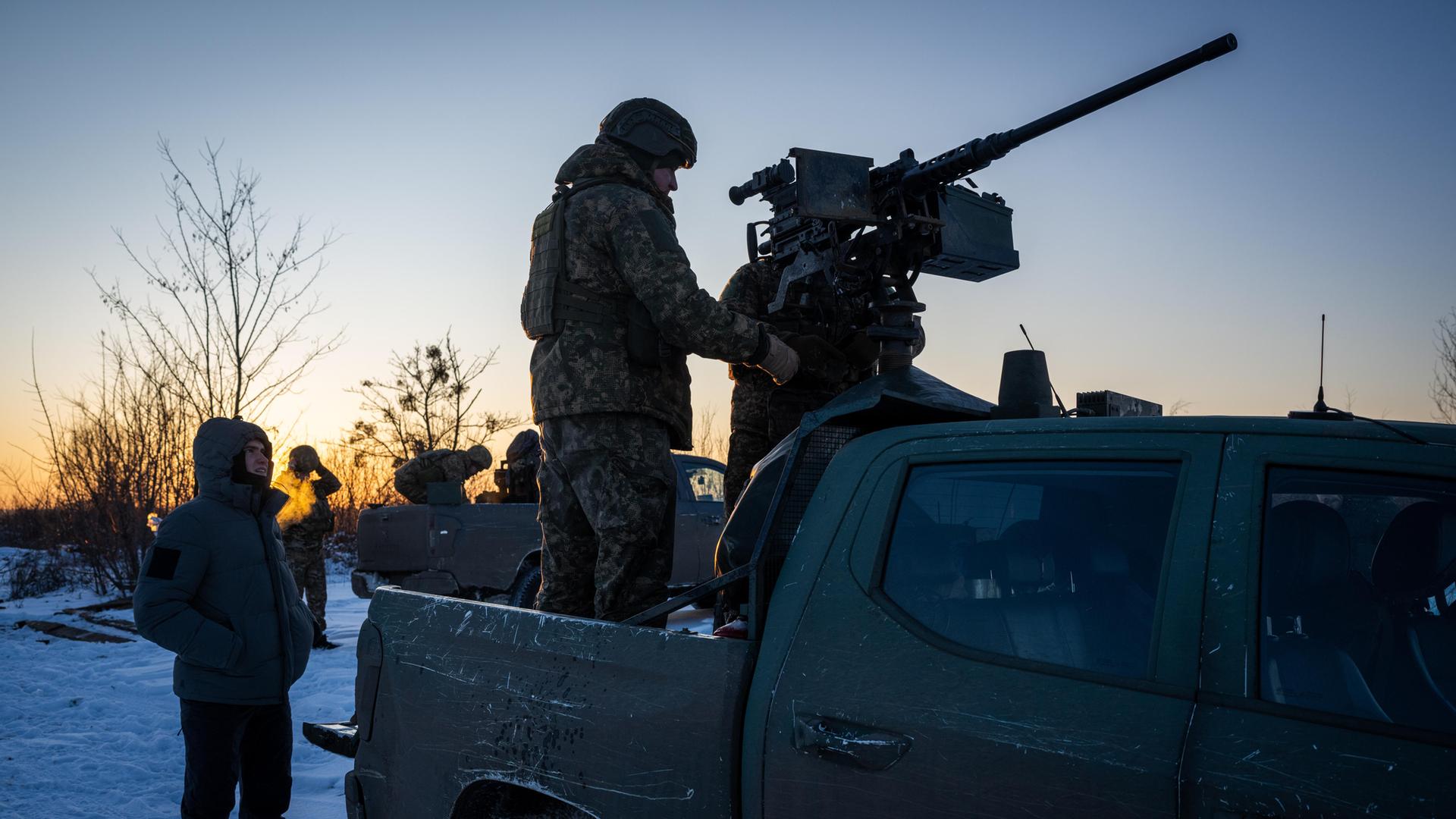 Schattenumriss von zwei Soldaten im Ukraine-Krieg: Der eine steht auf einem Fahrzeug und hantiert mit einer darauf montierten Waffe, der andere steht auf dem Boden und schaut dabei zu.