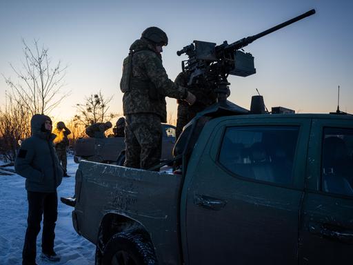 Schattenumriss von zwei Soldaten im Ukraine-Krieg: Der eine steht auf einem Fahrzeug und hantiert mit einer darauf montierten Waffe, der andere steht auf dem Boden und schaut dabei zu.