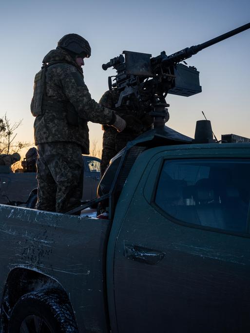 Schattenumriss von zwei Soldaten im Ukraine-Krieg: Der eine steht auf einem Fahrzeug und hantiert mit einer darauf montierten Waffe, der andere steht auf dem Boden und schaut dabei zu.