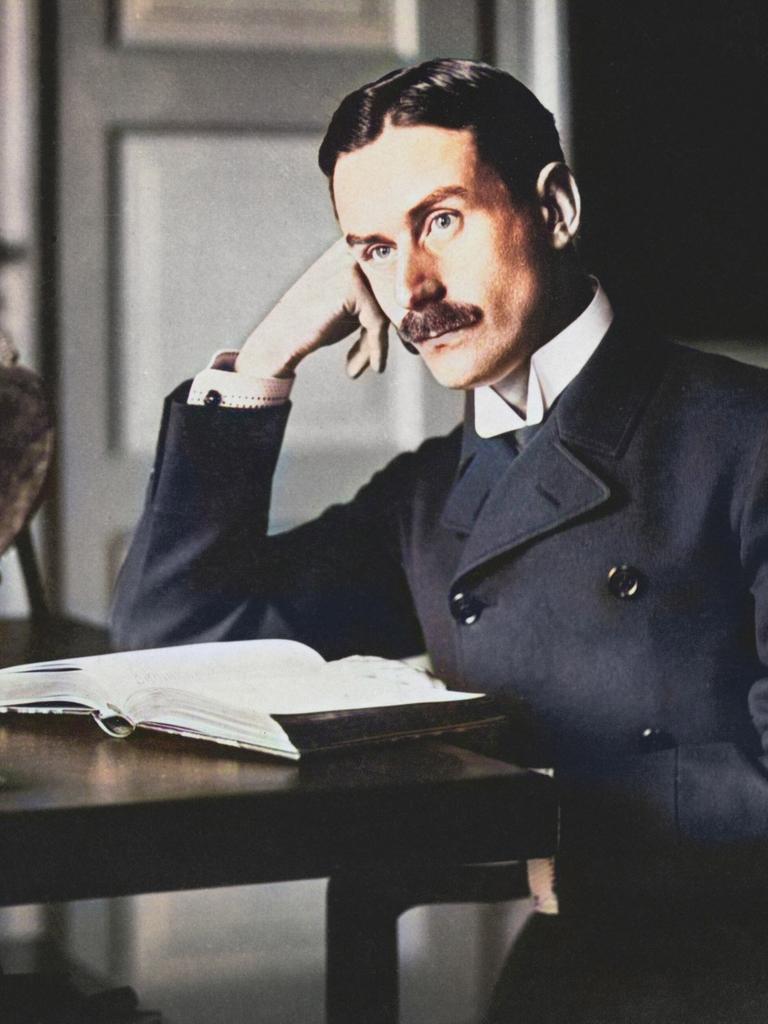 Thomas Mann sitzt an einem Tisch, den Kopf dabei in Hand gestützt. Nachkolorierte Fotografie.