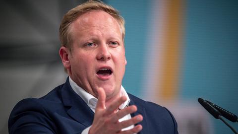 Tilman Kuban spricht in ein Mikrofon und gestikuliert mit der rechten Hand.