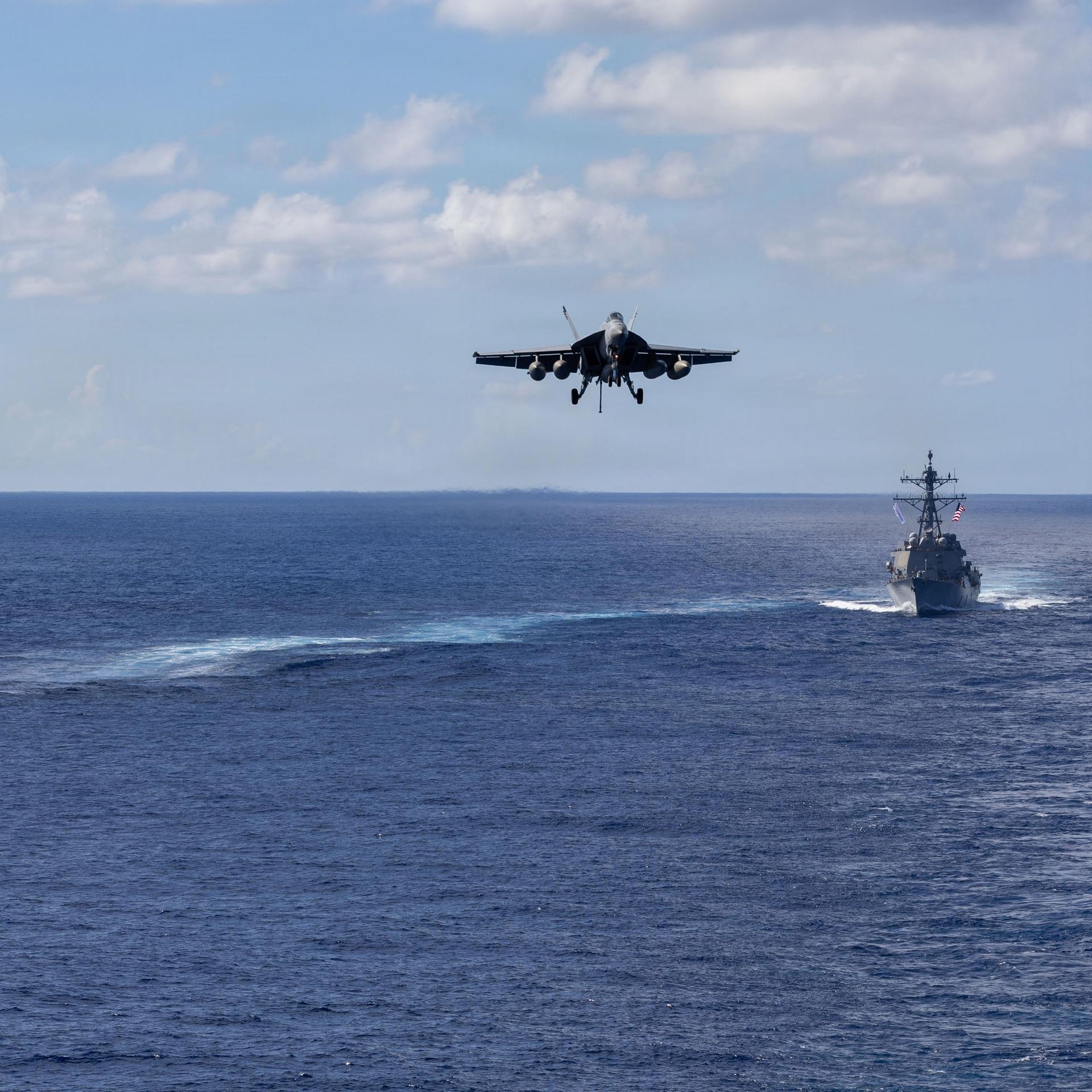 Die Lenkwaffenzerstörer der Arleigh-Burke-Klasse USS Mahan (l, DDG 72) und USS Bainbridge (DDG 96) fahren in Formation, während ein F/A-18 Super Hornet des Carrier Air Wing Eight zur Landung auf dem Flugzeugträger USS Gerald R. Ford (CVN 78) ansetzt. 